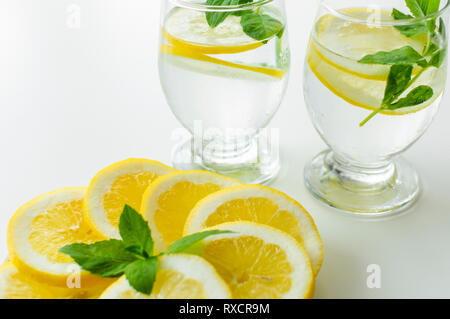 Deux boissons froides en verres transparents à côté assiette pleine de rondelles de citron avec des feuilles de menthe fraîche. Banque D'Images