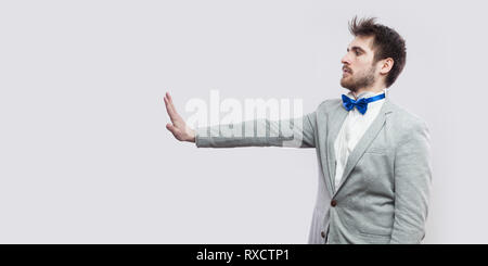 Vue côté profil portrait d'homme barbu beau graves occasionnels en costume gris, noeud papillon bleu et permanent à la geste de la main droite avec stop sign Banque D'Images