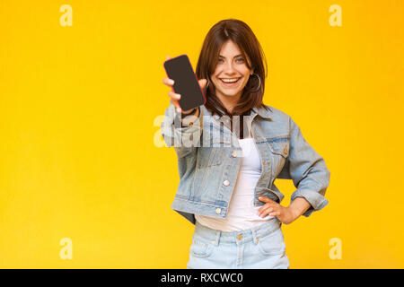 Portrait of happy beautiful brunette woman avec le maquillage en denim style décontracté, permanent à la caméra avec le sourire à pleines dents et montrant les di Banque D'Images