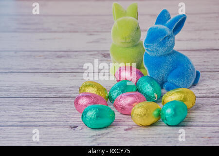 Deux lapins de Pâques colorés et de couleur chocolat à côté des oeufs sur un fond en bois blanc avec copie espace Banque D'Images