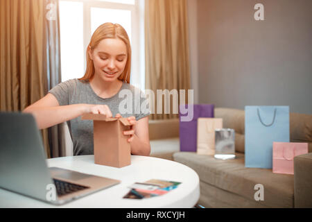 Magasinage en ligne à la maison. Young smiling shopper est unboxing sa parcelle, commandés par internet, alors qu'il était assis à la table Banque D'Images