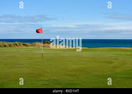 Golf rouge sur le drapeau vert à la coastal golf avec vue sur la mer en arrière-plan, Port Fairy Victoria Australie Banque D'Images