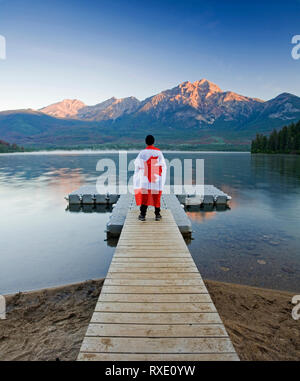 Homme avec drapeau canadien marche sur un quai dans le lac Pyramid, Jasper National Park, Alberta, Canada. Banque D'Images