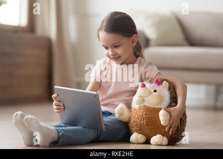 Enfant curieux girl having fun using digital tablet embrassant toy