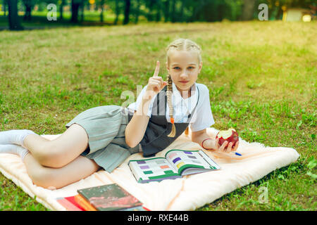 Lycéenne en uniforme montre un certain nombre de doigts, signe d'attention. l'étudiant est en train de manger le déjeuner dans le parc et l'apprentissage des leçons. petite fille hol Banque D'Images