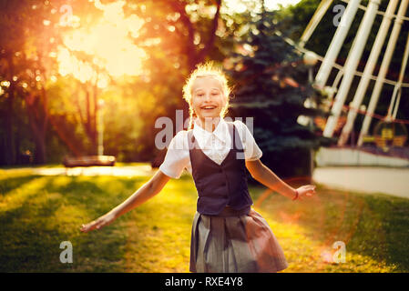 Lycéenne en uniforme avec des nattes danse joyeuse au coucher du soleil dans la lumière du soleil dans le parc. étudiante jouit du vacations Banque D'Images