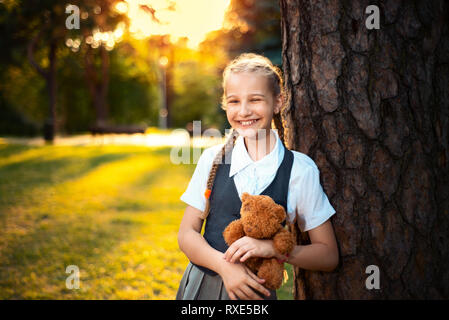 Lycéenne en uniforme, rires et sourires. l'adolescent est holding a soft toy ours au coucher du soleil Banque D'Images