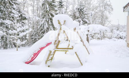 Un toboggan et une balançoire recouverte de neige. Toute la pelouse et aire de jeux est recouverte de neige pendant la saison d'hiver Banque D'Images