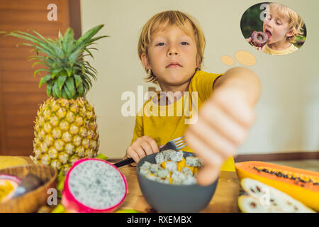 Garçon mange des fruits mais rêve de beignets. Aliments sains et nocifs pour les enfants. Enfant de manger une collation. L'alimentation végétarienne pour les enfants. Des vitamines pour Banque D'Images