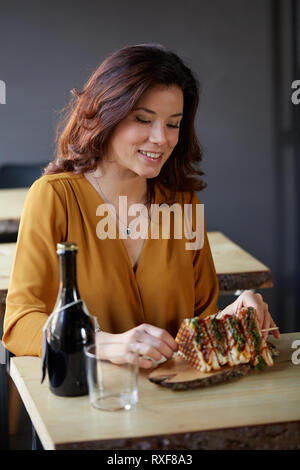 Belle femme manger un club sandwich à l'intérieur d'un pub Banque D'Images