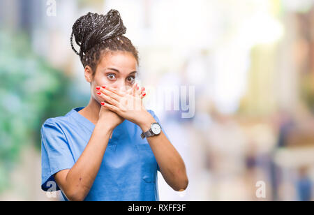 Les jeunes cheveux tressés african american girl infirmière professionnelle sur fond isolé choqué couvrant la bouche avec les mains pour l'erreur. Concept Secret. Banque D'Images