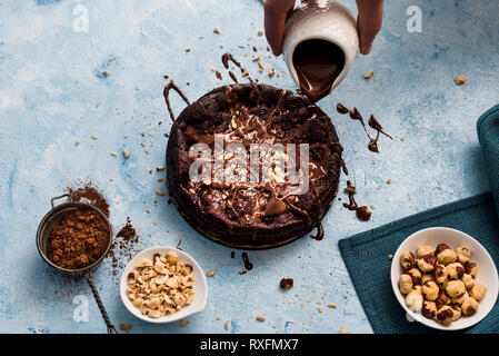 Verser le chocolat sur un gâteau au chocolat avec des noisettes sur un fond texturé bleu Banque D'Images