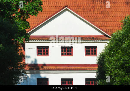 Maison avec pignon blanc et rouge les tuiles terre entourée d'arbres verts Banque D'Images