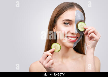 Femme avec masque facial et tranches de concombre dans ses mains sur fond blanc Banque D'Images