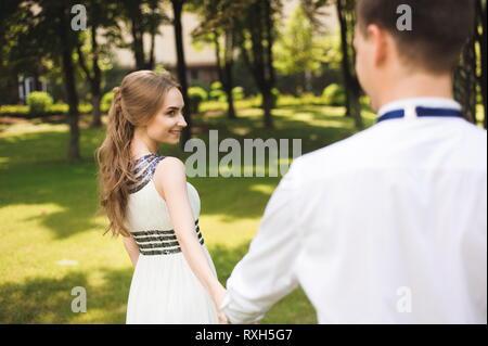 Couple en tenue de mariage est dans les mains sur la toile de fond le terrain au coucher du soleil, la mariée et le marié Banque D'Images