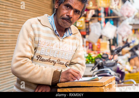 A middle aged Indian man wearing sweater debout, regardant la caméra et un ordinateur portable a ouvert l'après-midi en hiver. Il est 50-55 ans. Banque D'Images