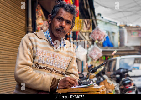 A middle aged Indian man wearing sweater debout, regardant la caméra et un ordinateur portable a ouvert l'après-midi en hiver. Il est 50-55 ans. Banque D'Images