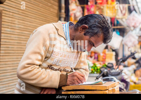 A middle aged Indian man wearing sweater debout, regardant vers le bas et d'écrire quelque chose sur un ordinateur portable dans l'après-midi en hiver. Il est 50-55 ans. Banque D'Images