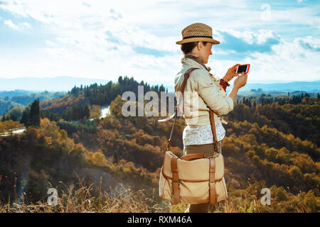 Vus de derrière, les jeunes touristes en solo femme d'équipement de randonnée avec sac et smartphone à l'aide d'applications sur la route d'été en Toscane. Banque D'Images