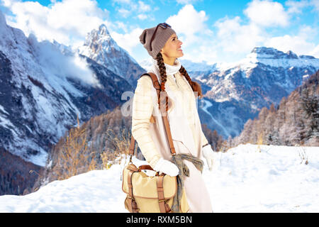 Smiling femme saine en veste blanche avec des lunettes de soleil à l'avant de paysages de montagne dans l'Alto Adige, Italie recherche dans la distance. Banque D'Images