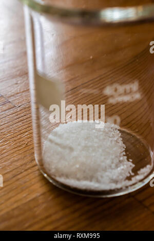 Petit verre de 40 mL bécher chimie avec de petits cristaux de sucre géométrique fixant dans le fond. Profondeur de champ tourné à se concentrer sur les cristaux. Banque D'Images