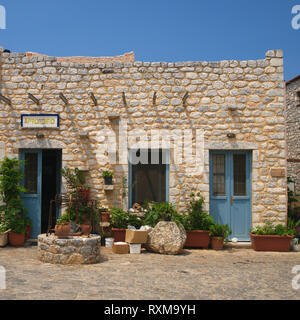 Boulangerie en pierre aux portes bleues sur une place pavée avec de l'eau bien dans un village grec dans le magne, Grèce. Banque D'Images