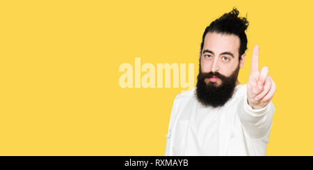 Jeune homme hipster avec de longs cheveux et barbe portant des sweat sportive avec le doigt pointant vers le haut et l'expression de colère Banque D'Images