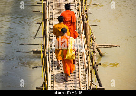 Trois moines bouddhistes non identifiés sont la traversée du pont de bambou qui s'exécutent sur la rivière Nam Khan. Banque D'Images