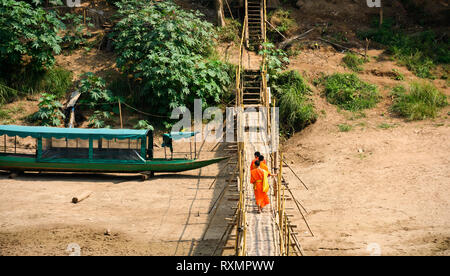 Trois moines bouddhistes non identifiés sont la traversée du pont de bambou qui s'exécutent sur la rivière Nam Khan. Banque D'Images