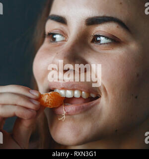 Cute girl eating ludique sweet mandarine. Close up Banque D'Images