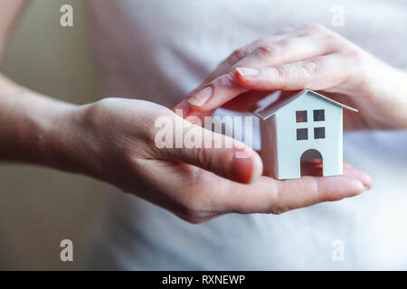 Female woman hands holding petit blanc miniature toy house. L'assurance des biens hypothécaires dream déménagement accueil concept et de l'immobilier Banque D'Images