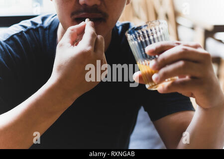 La dépression qui prend des pilules avec verre d'alcool. Banque D'Images