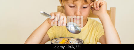 Heureux garçon assis et mangeant un smoothie frais bol avec de la mangue, fruit du dragon, granola et chia seeds BANNER, format long Banque D'Images