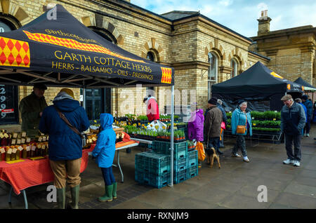 Les personnes bénéficiant de soleil du printemps dans un coin abrité du mensuel du marché des agriculteurs par la station à Saltburn by the sea North Yorkshire Banque D'Images