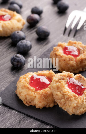 Cookies faits de shortcake aux noisettes avec de la confiture de fraise à l'intérieur sur une serviette noire avec des bleuets et une fourchette à dessert à motifs sur un fond sombre n Banque D'Images