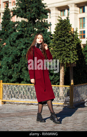 Portrait complet du corps. Belle jeune femme brune en élégant dans un long manteau bourgogne walking in spring street Banque D'Images