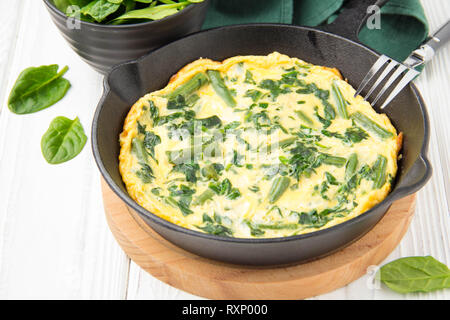 Omelette aux épinards et haricots, alimentation saine. L'oeuf et le lait Frittata, délicieux petit-déjeuner. Poêle en noir sur blanc fond de bois Banque D'Images