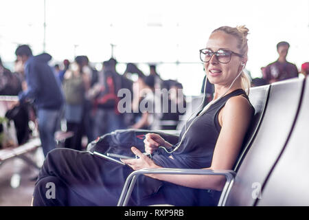 Female traveler en utilisant son téléphone portable en attendant de monter à bord d'un avion à l'embarquement au terminal de l'aéroport d'Asie. Banque D'Images