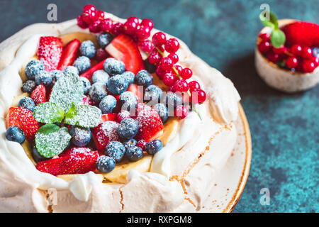 La NOUVELLE ZELANDE Pavlova gâteau avec la crème fouettée et mélange de baies fraîches sur un fond texturé bleu. Banque D'Images