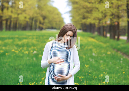 Portrait d'un heureux et fiers à la femme enceinte à son ventre dans un parc en journée ensoleillée Banque D'Images