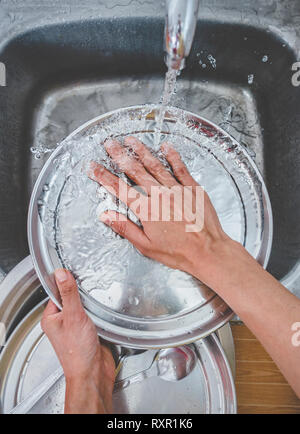 Vue perspective personnelle des mains laver les ustensiles au-dessus de l'évier dans la cuisine Banque D'Images