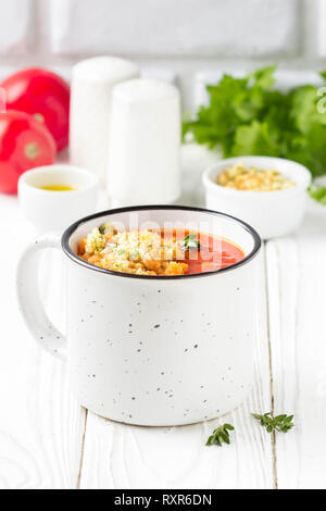 Soupe crème de tomates en blanc mug, rouge soupe chaude dans la tasse de chapelure et d'huile d'olive. Déjeuner légumes végétarien sur fond de bois Banque D'Images