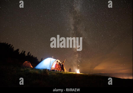 Nuit de camping d'été dans les montagnes près de la forêt. Couple heureux randonneurs ayant un reste ensemble, assis dans la tente à côté d'un feu de camp. Man Po Banque D'Images