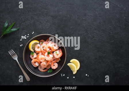 Les crevettes dans un bol, vue du dessus, copiez l'espace. Des fruits de mer contexte - queues de crevettes sur noir. Gambas et baguettes. Banque D'Images