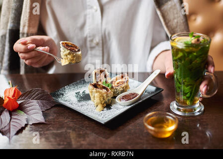 Fille de récolte en blanc verre en main et portefeuille manger sucré délicieux sushi roll avec sauce au chocolat. Recouverte de détente générale avec les desserts et Banque D'Images