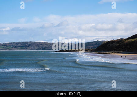 Benllech, Isle of Anglesey, au nord du Pays de Galles, Royaume-Uni. 10 Mar 2019. Rouleau de vagues sur la plage de Benllech à sunshine sur un jour venteux froid avec de la neige sur les lointaines montagnes de Snowdonia. Le week-end a vu le vent froid changeant à travers l'île. Une tempête suivie peu après. Credit : Realimage/Alamy Live News Banque D'Images