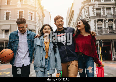 Jeunes amis asiatiques à marcher ensemble dans la rue. Groupe de quatre personnes marchant avec des planches à roulettes et de basket-ball. Banque D'Images