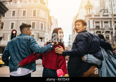 Vue arrière des amis à marcher ensemble à l'extérieur avec les bras autour, avec le couple à l'arrière. Groupe d'hommes et femmes d'Asie hanging out. Banque D'Images