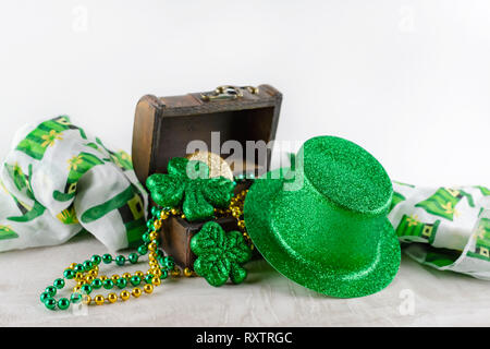 Saint Patrick's Day top hat appuyé contre un coffre au trésor rempli de perles, pièces de monnaie, et des trèfles. Foulard coloré à l'arrière-plan. Bac blanc Banque D'Images