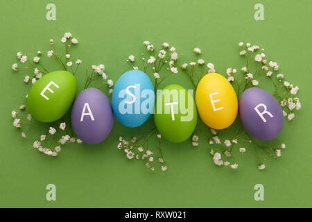 Les oeufs peints colorés avec des lettres disposées en un mot Pâques avec des fleurs sur fond vert. Concept de vacances de printemps. Banque D'Images